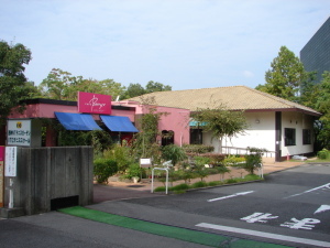 入り口から入って左側に桃色の看板と外壁の「カフェ ベリー 西神ニュータウンテニスガーデン」があり、奥に白い外壁の建物が続いている西神ニュータウンテニスガーデン入り口前の写真