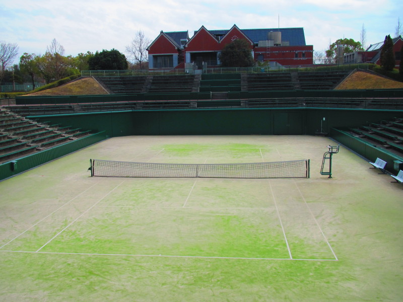 テニスコートを囲むように観覧席が設置されている総合運動公園センターコートとテニスコートの上に見えるクラブハウスの写真